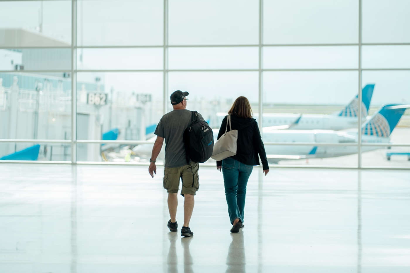Two travelers with luggage arriving at the airport, planes visible through the windows