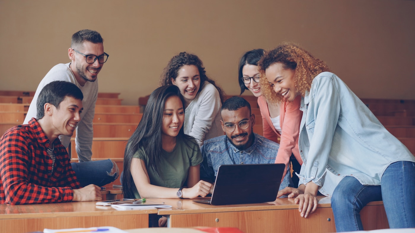 A diverse group of students studying together around a laptop