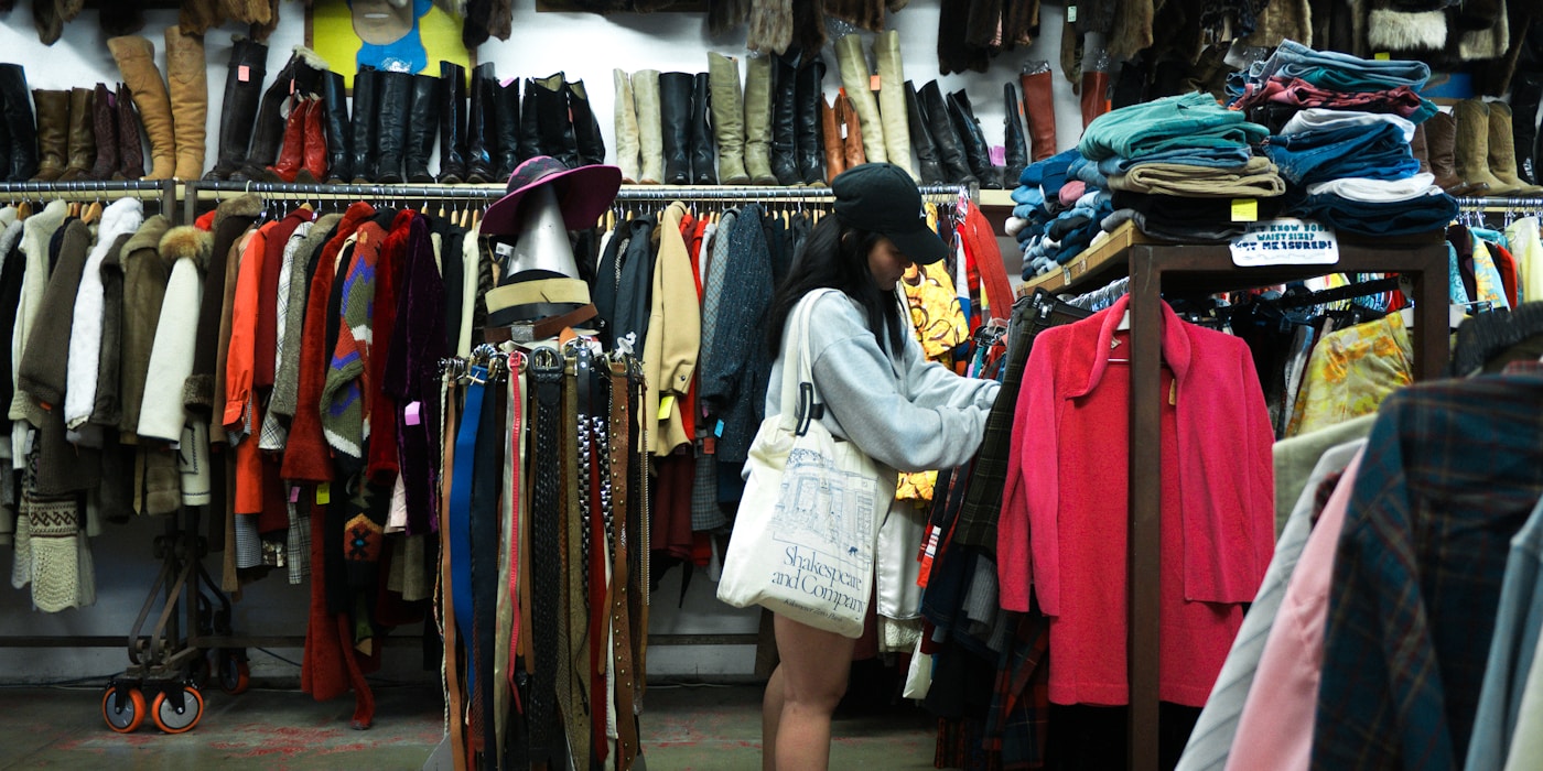 Someone browsing racks of coats and clothes in a thrift store