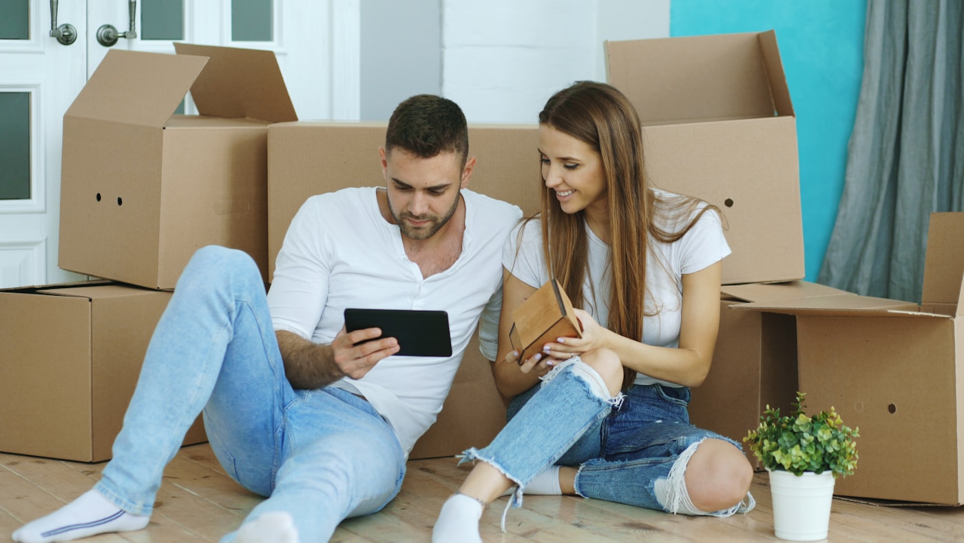 A couple sitting among moving boxes in a new apartment, checking a budget on a tablet